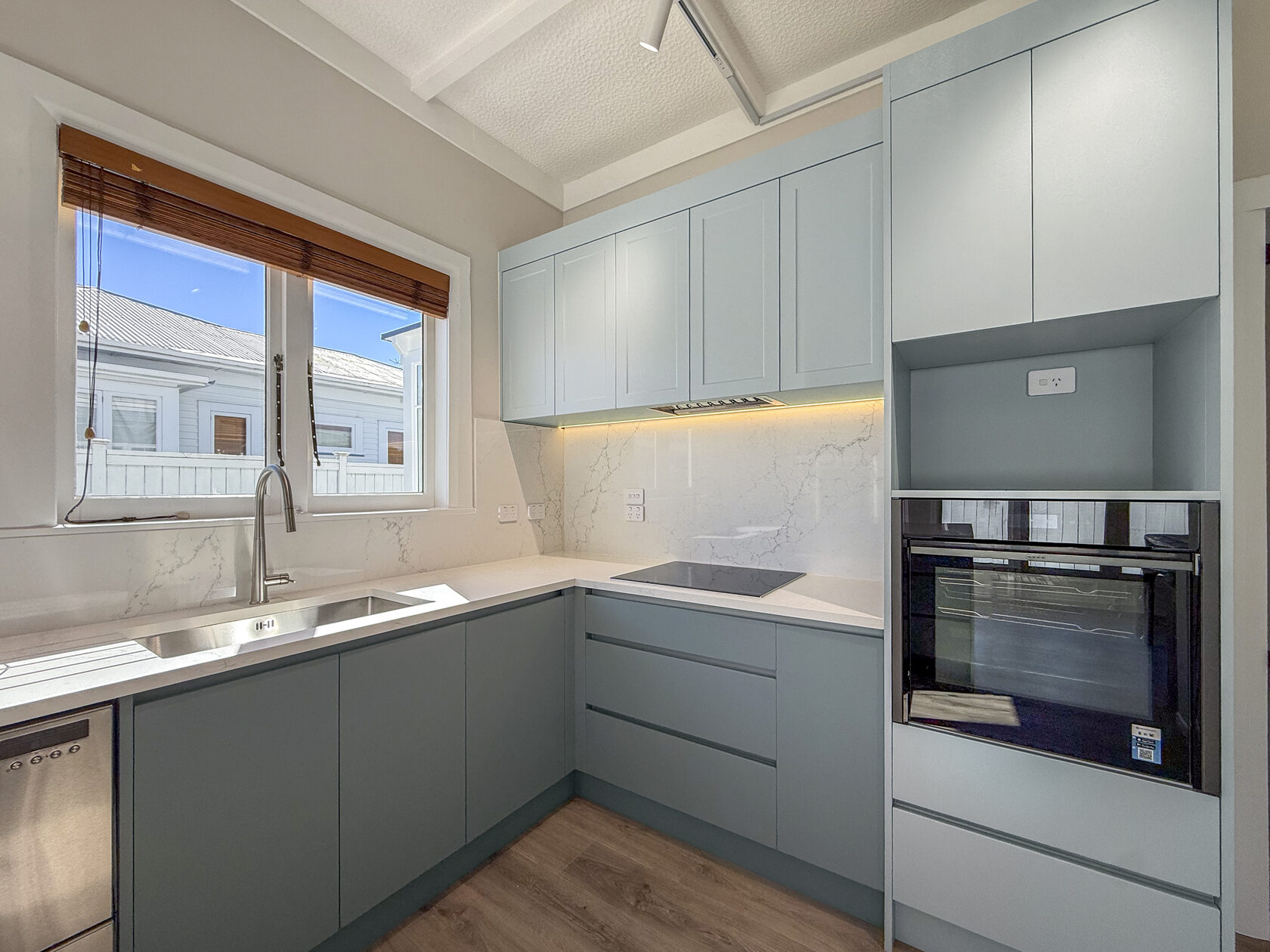 Muted green kitchen cabinets and pale worktops in the renovated bungalow