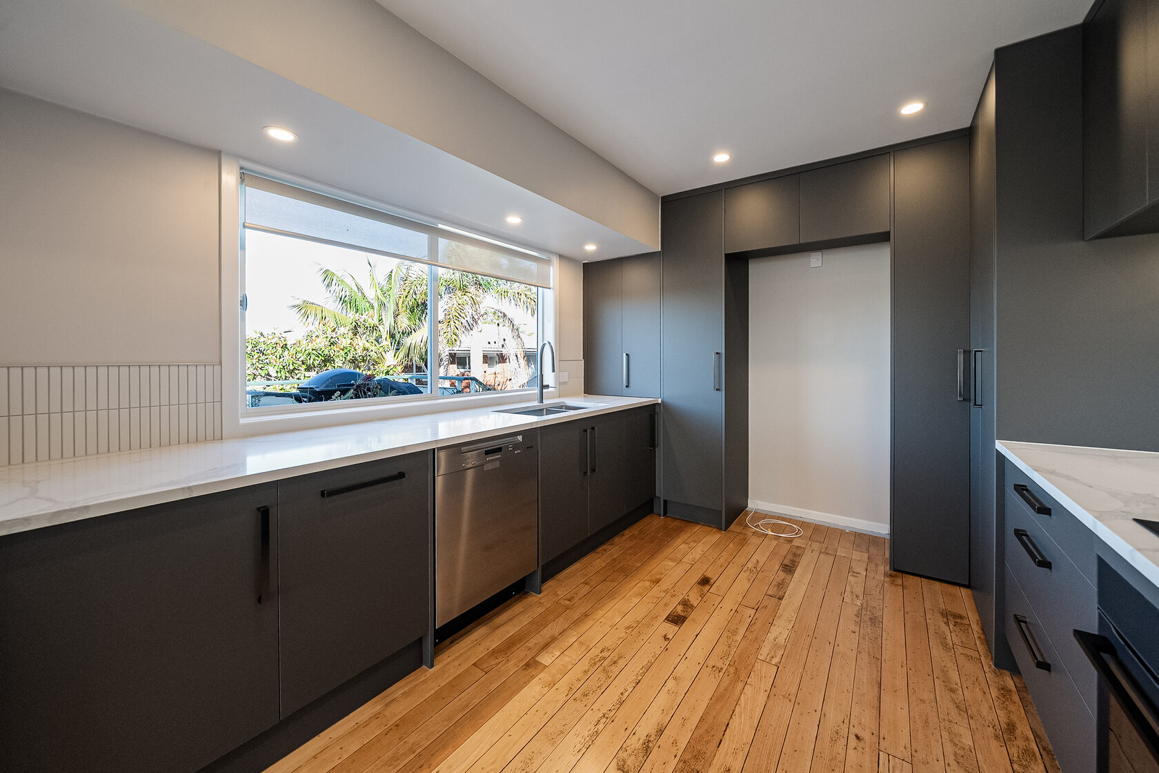 Renovated Glenfield kitchen with dark cabinetry, pale benchtops and a wide garden-facing window