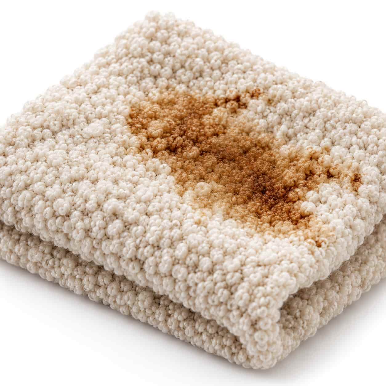 Nahaufnahme von cremewei&szlig;em Boucl&eacute; mit einem braunen Kaffeefleck zwischen den Garnschlingen auf wei&szlig;em Hintergrund. Shikardos Reinigung saugt solche Flecken in Frankfurt mit wenig Druck aus den Zwischenr&auml;umen.