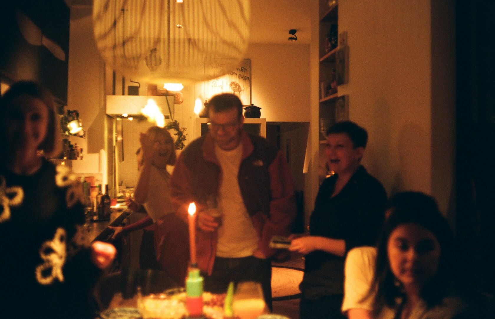 A small group of friends laughing around a long candlelit dinner table in an olive grove