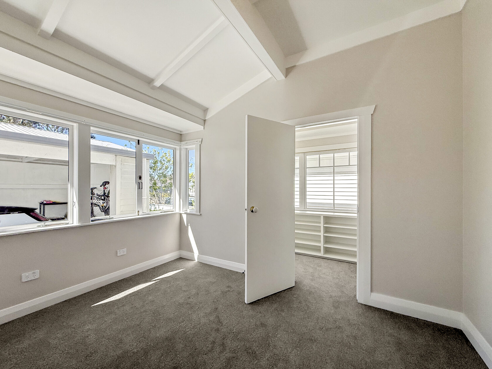 Bright carpeted room with white walls, timber-framed windows and a doorway