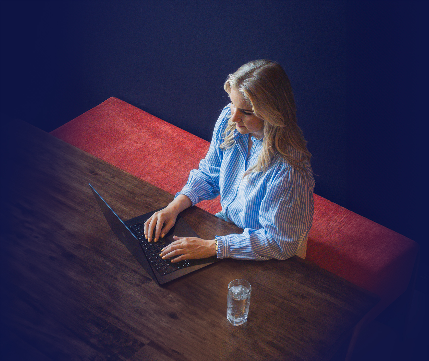 Femke Teunissen zit op bankje achter bureau met laptop