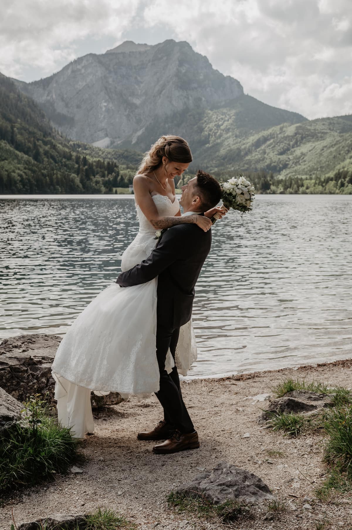 Groom lifting bride by a mountain lake in the Austrian Alps, joyful wedding portrait
