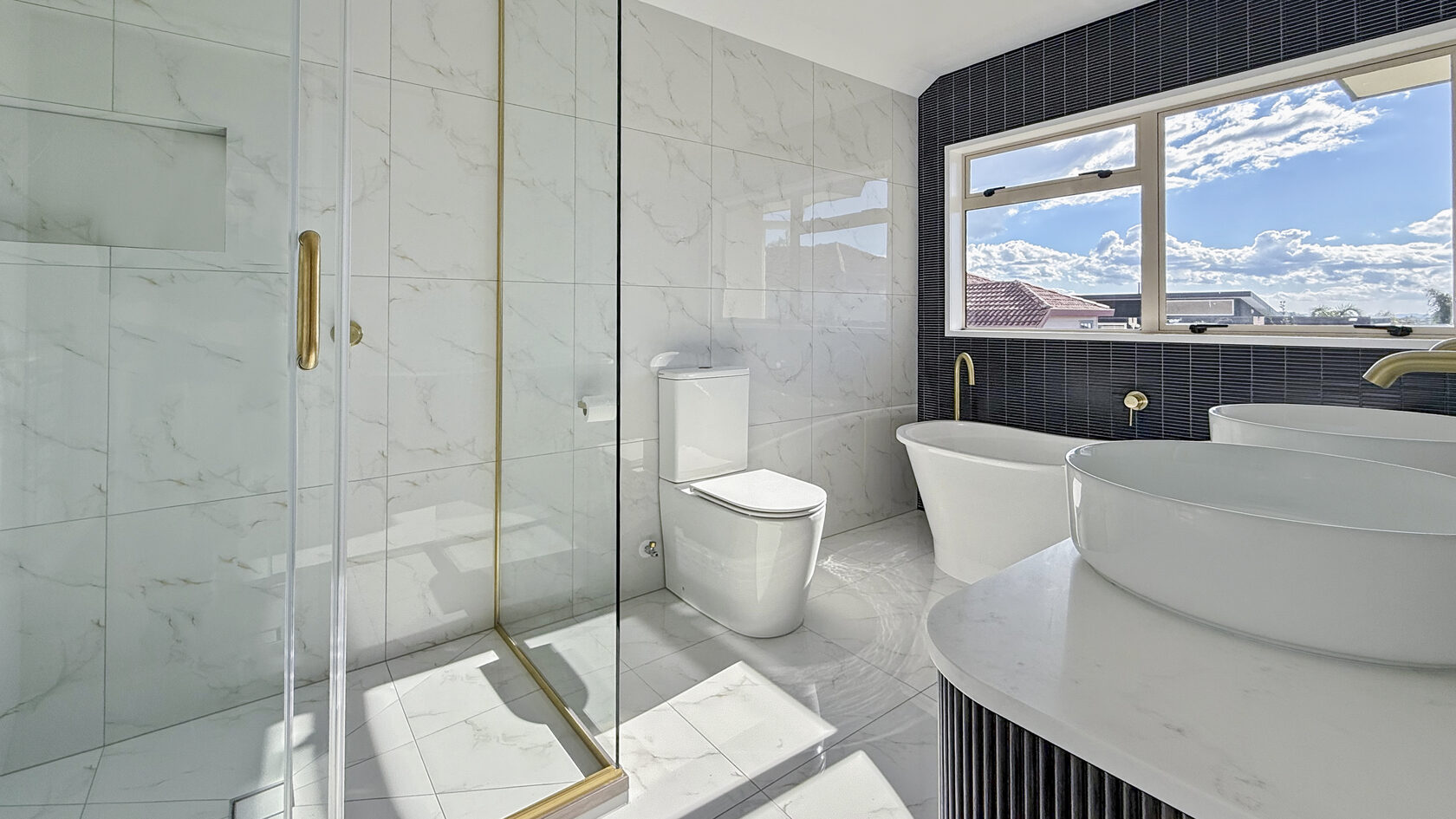 St Heliers bathroom with freestanding bath, glass shower, double vanity and brass fixtures.