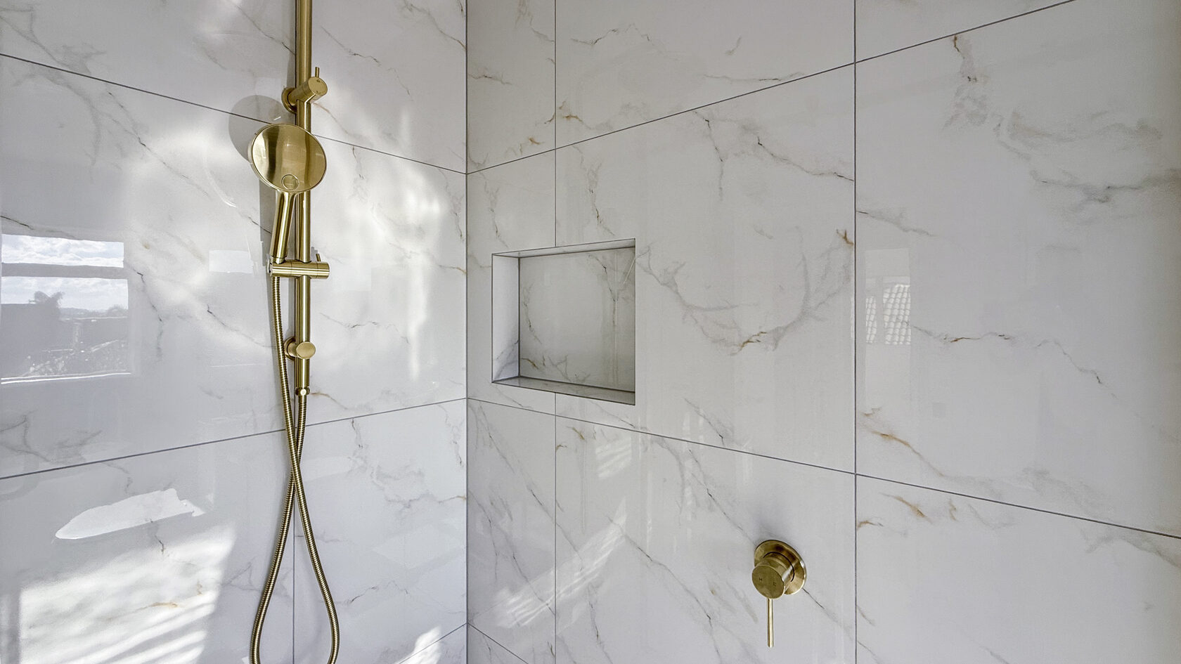Brushed brass handheld shower and built-in wall niche in the St Heliers bathroom.
