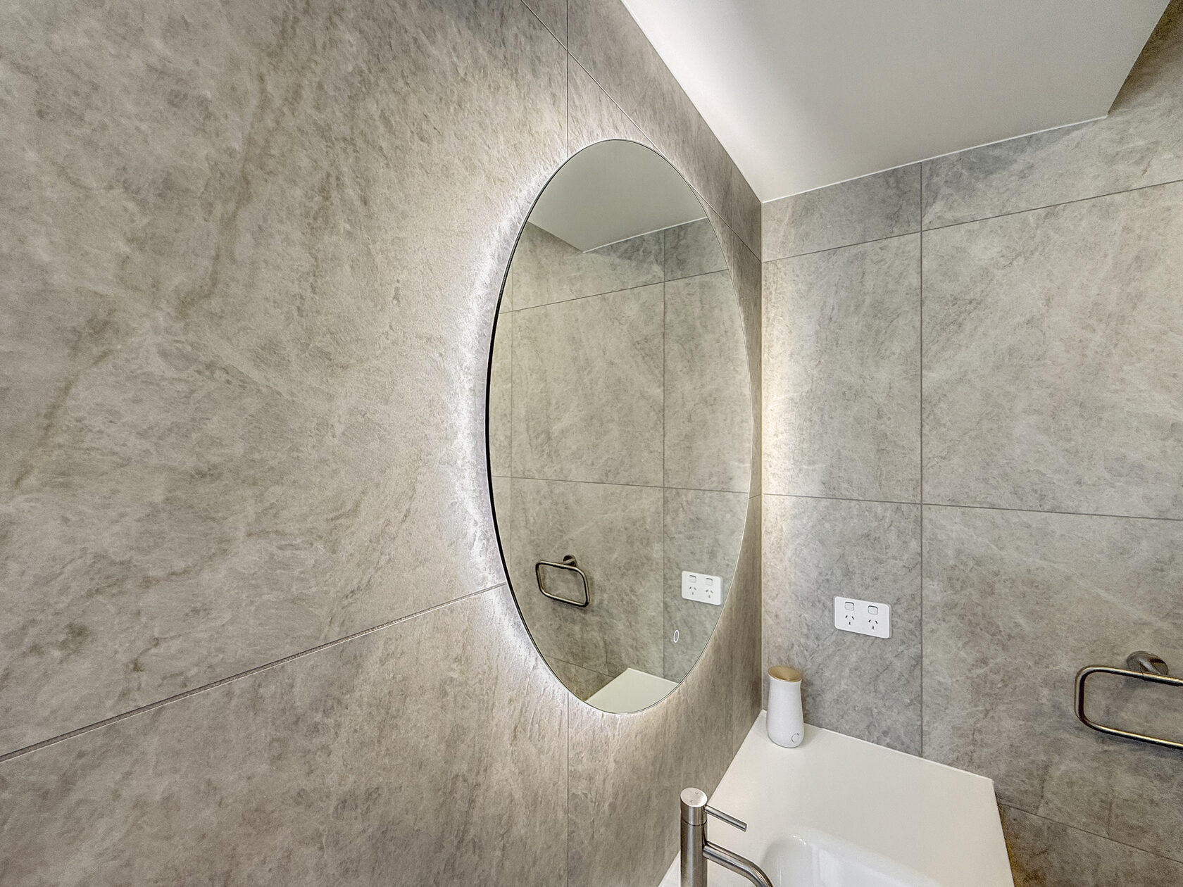 Close view of an illuminated round mirror above the bathroom vanity