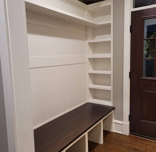 Mudroom shelves and built-in dark stained bench furnished with baskets and hooks 