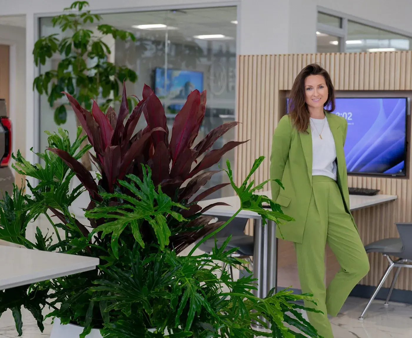 Layered burgundy and green planter composition at a corporate reception desk, with a team member standing beside it