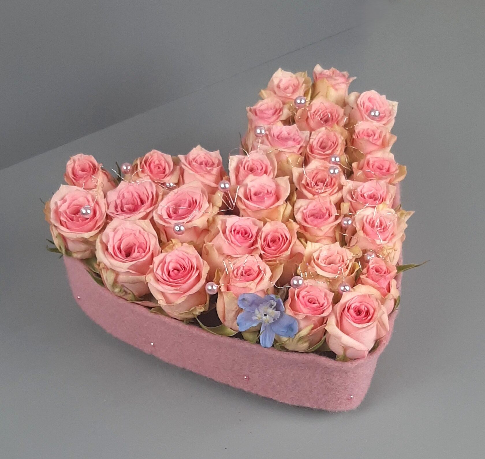 A floral arrangement of soft pink roses in a heart-shaped velvet box.