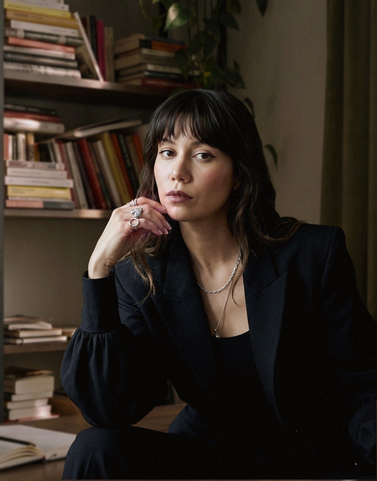 Gulnaz Ratu in a black blazer, chin resting on her hand, in front of a bookshelf