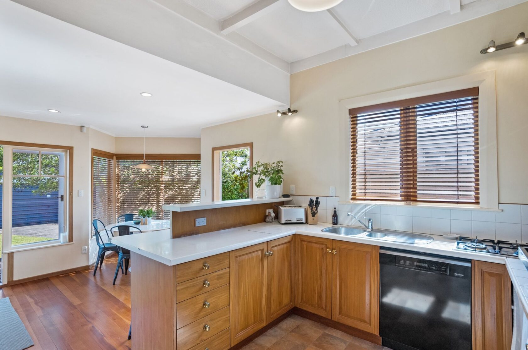 Before renovation: kitchen with timber cabinetry, white benchtops and an adjoining dining area
