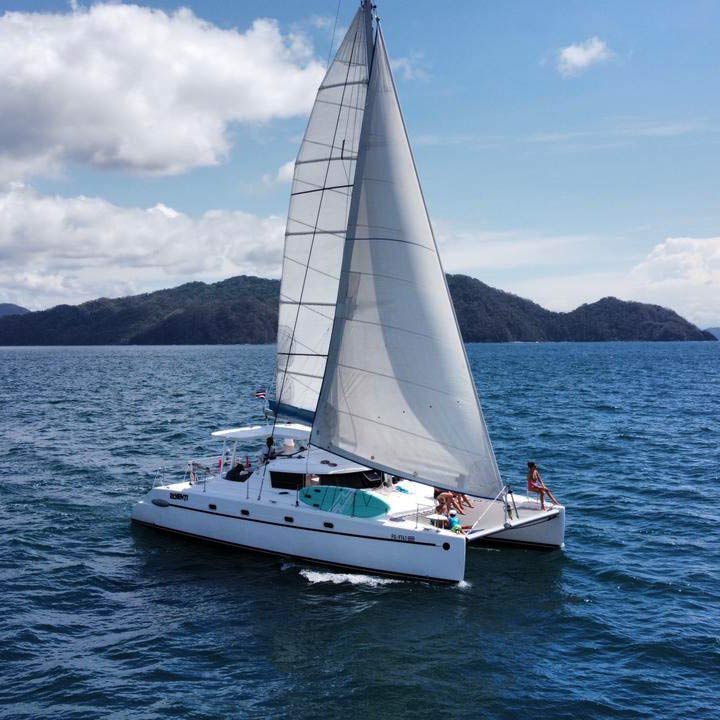 Catamarán blanco a toda vela en el mar azul con huéspedes en cubierta