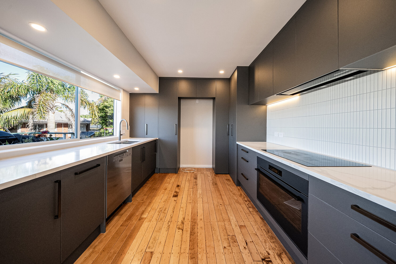 Renovated Glenfield kitchen with dark cabinetry, a long worktop and timber flooring