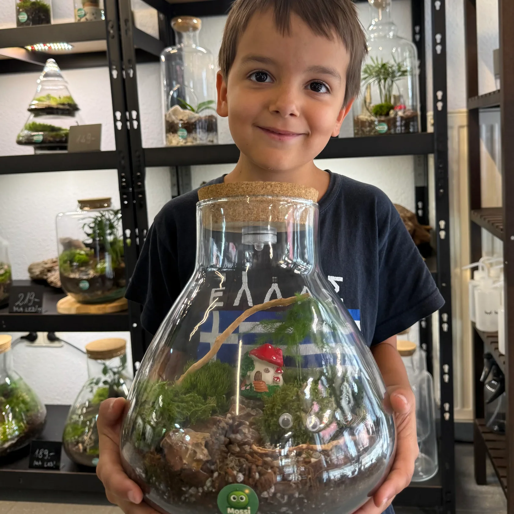 Kind hält stolz sein selbst gebautes Biotop im Glas mit Moos, Farn und Pilz in den Händen – Kindergeburtstag bei IZSO NaturArt in Lahr