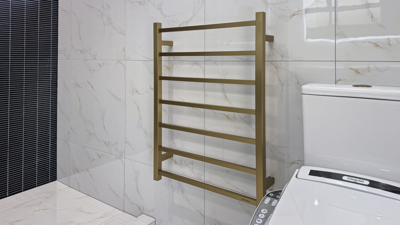 Brushed brass heated towel rail beside a smart toilet in the St Heliers bathroom.
