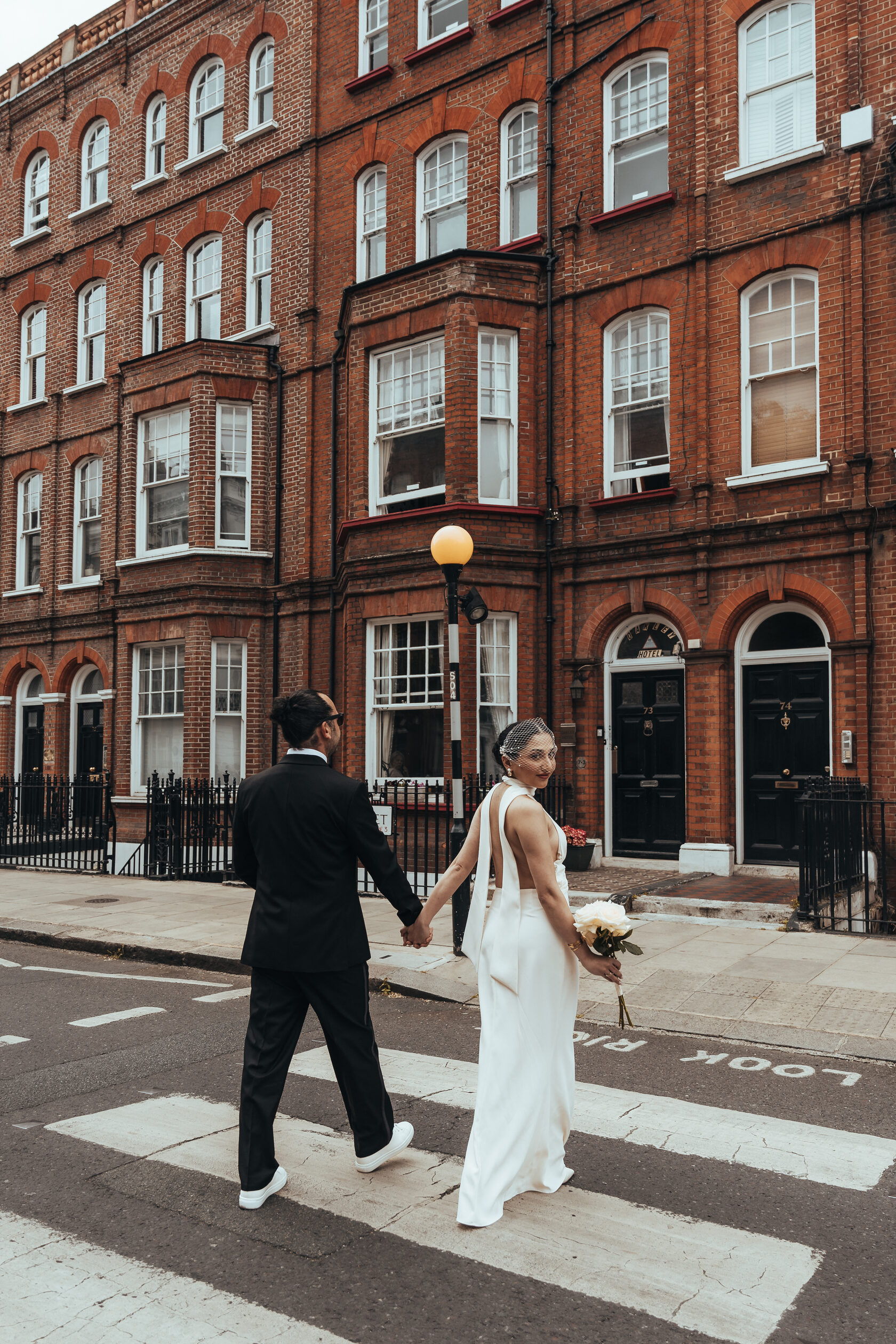 A couple walking together across a London street lined with red-brick buildings