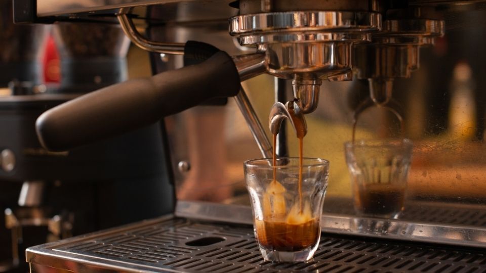 The image shows a professional espresso machine brewing a double espresso into a glass cup. High-quality water is essential for extraction, affecting the taste, acidity, and balance of coffee.