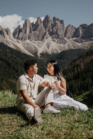 Couple sitting on a grassy hilltop with panoramic mountain views — quiet connection in the Dolomites