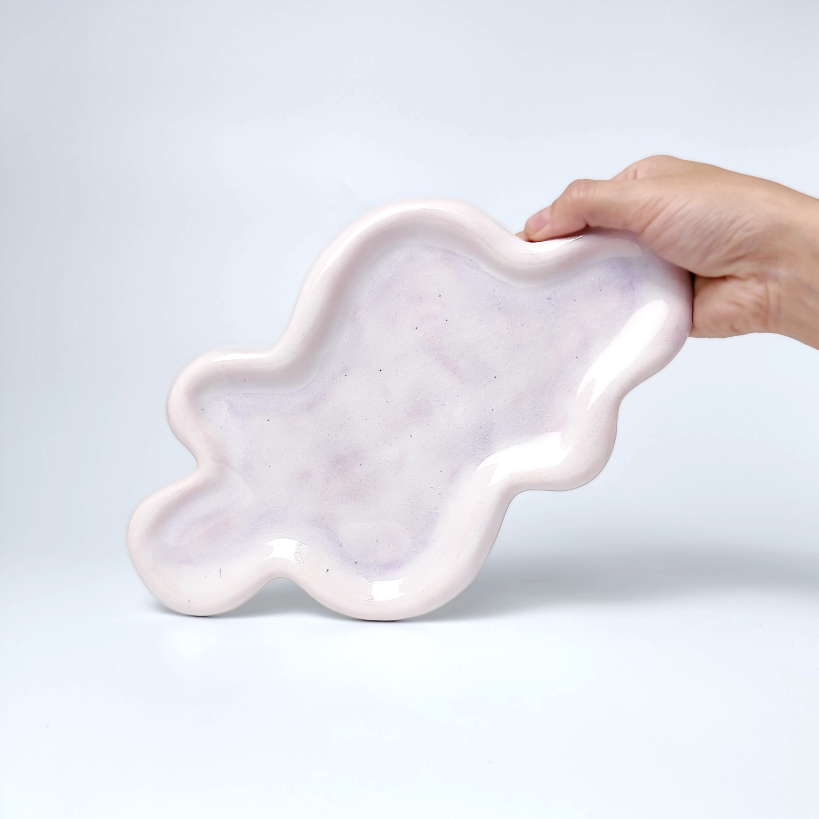 Unique handmade ceramic plate shaped like a cloud, featuring soft pastel pink glazing and an organic sculptural form