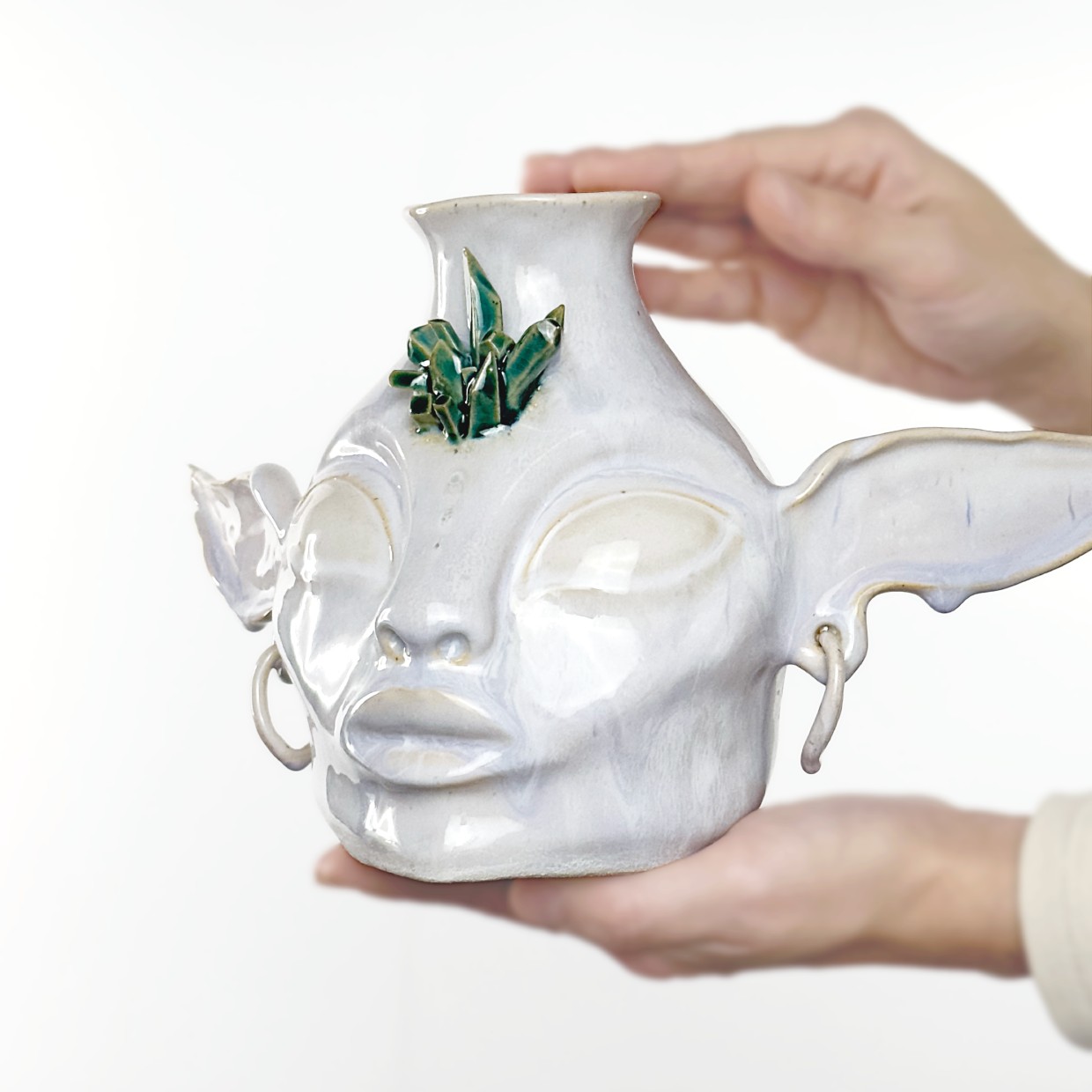 Unique handmade ceramic vase in the shape of a fantasy-inspired face with elongated ears and large hoop earrings. The surface is glazed with a pearlescent finish and a soft lavender sheen. Turquoise crystal-like elements on the forehead add a mystical, fairy-tale character to the piece. Its smooth texture, expressive facial features, and sculptural details make this vase a striking art object for interior decor. Perfect for dried flowers, decorative branches, or as a standalone magical accent