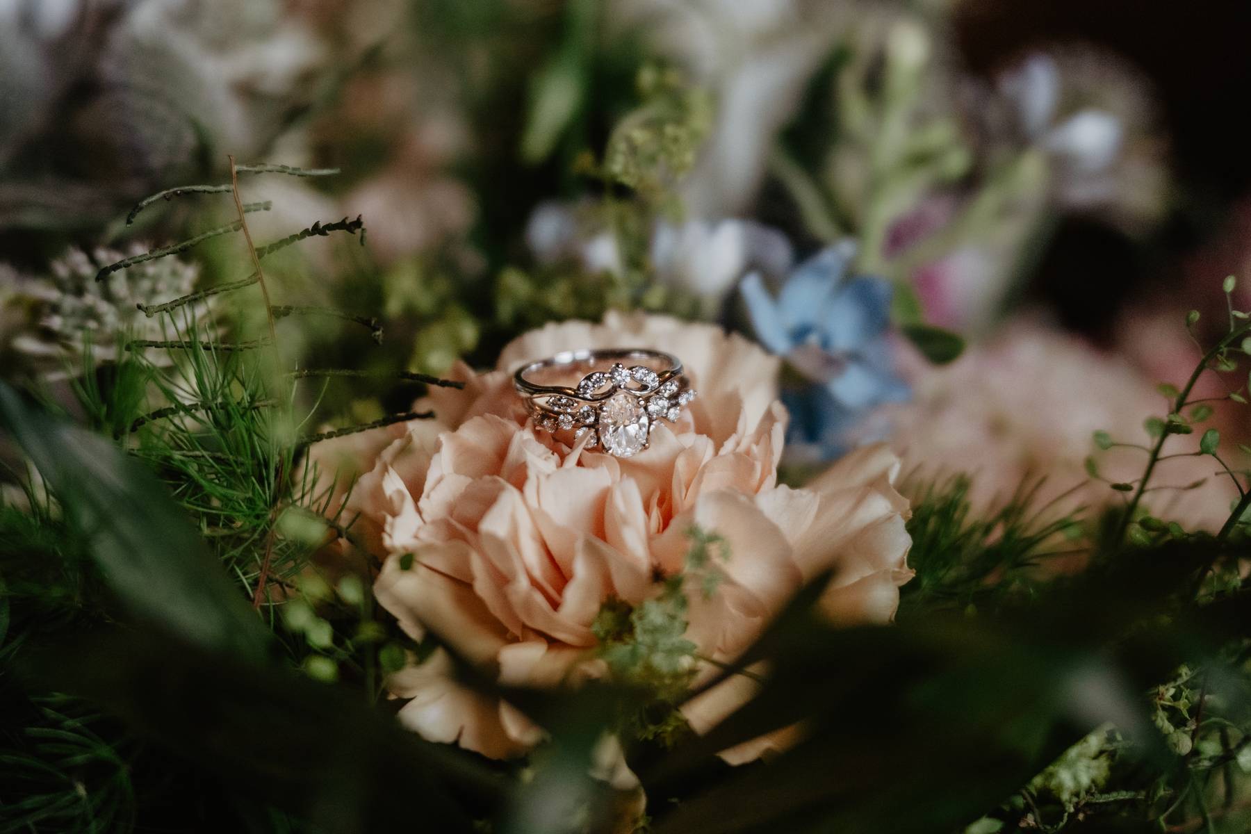 Diamond engagement ring resting among soft oeach roses and greenery in a romantic wedding bouquet