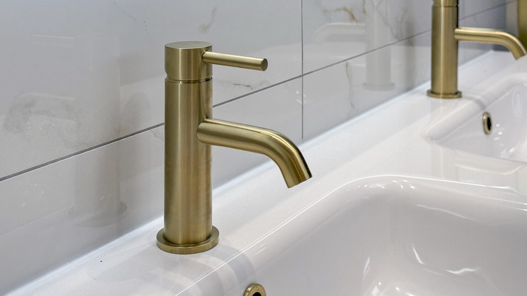Close view of brushed brass basin taps against marble-look bathroom tiles in St Heliers.