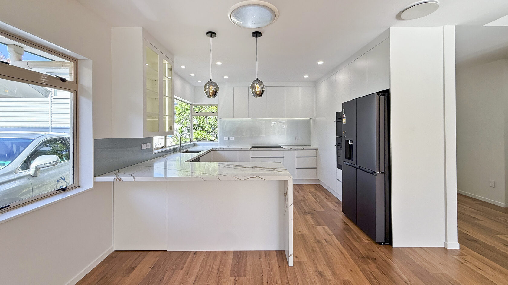 After: completed St Heliers kitchen in the Eastern Bays with white cabinetry, stone-look benchtops and pendant lighting