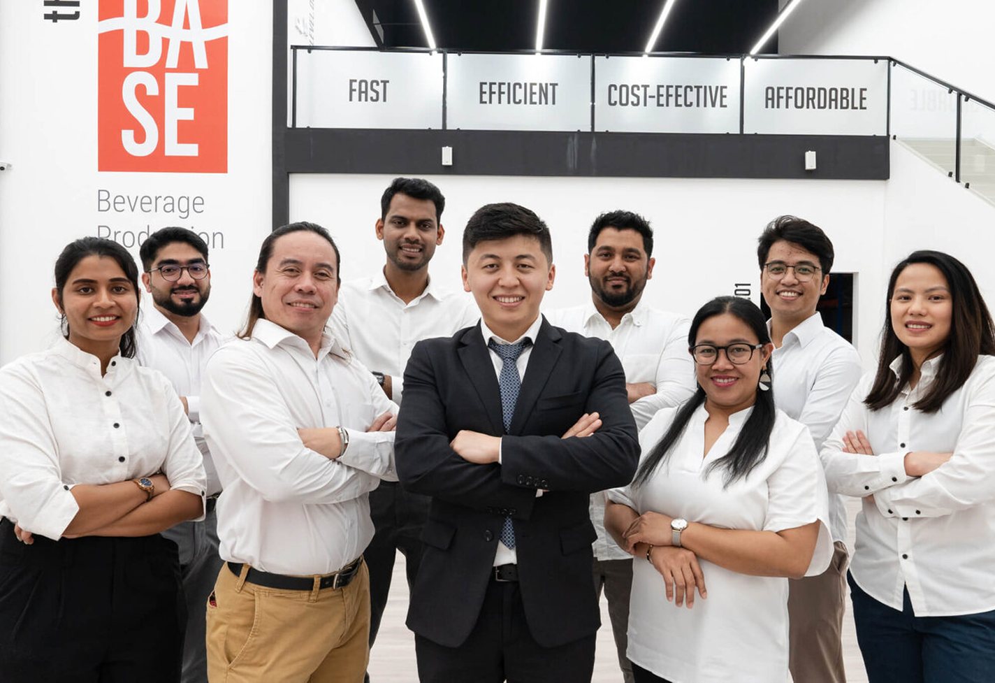 The Base Beverage team at the Dubai production facility in front of the Fast, Efficient, Cost-effective, Affordable wall