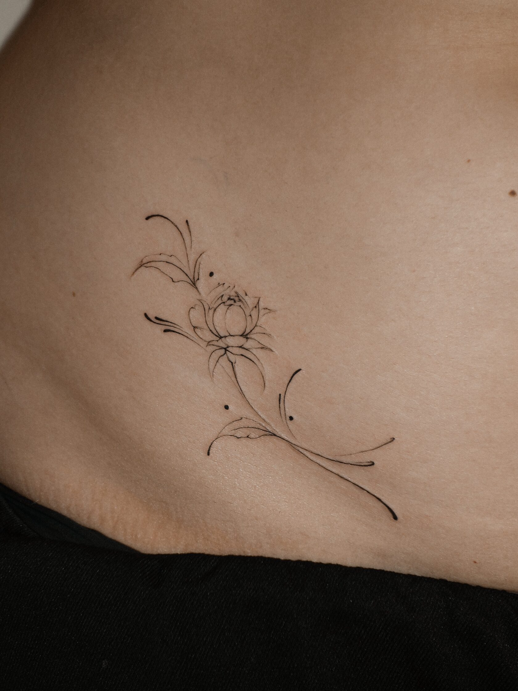 Small botanical flower tattoo with fine outlines, curved lines and individual dots by @zaitceva.ana