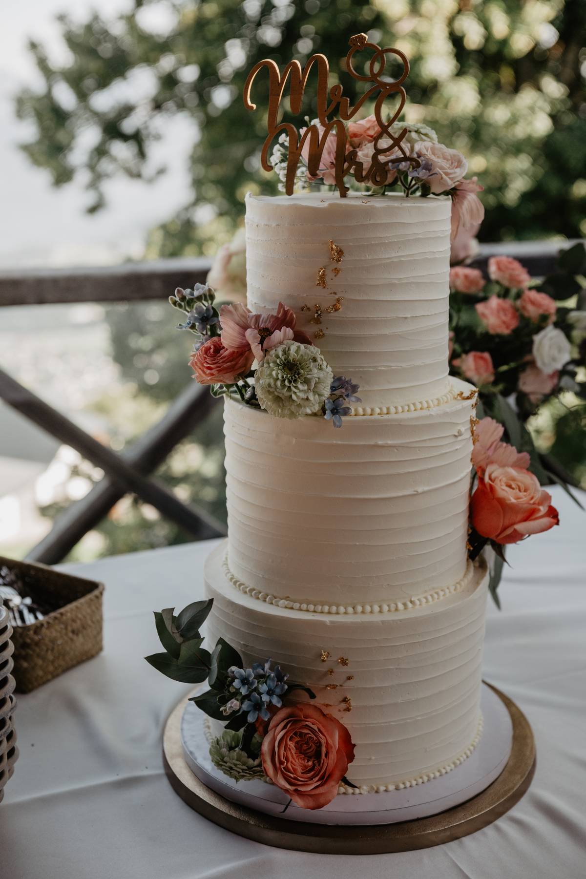 Two-tier wedding cake with floral decorations and “Mr &amp; Mrs” topper on the reception table