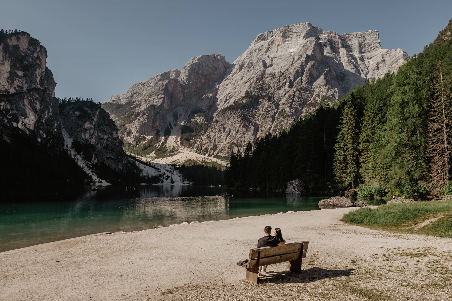 Couple sitting on a bench by an alpine lake in the Dolomites, Italy, with towering peaks in the background