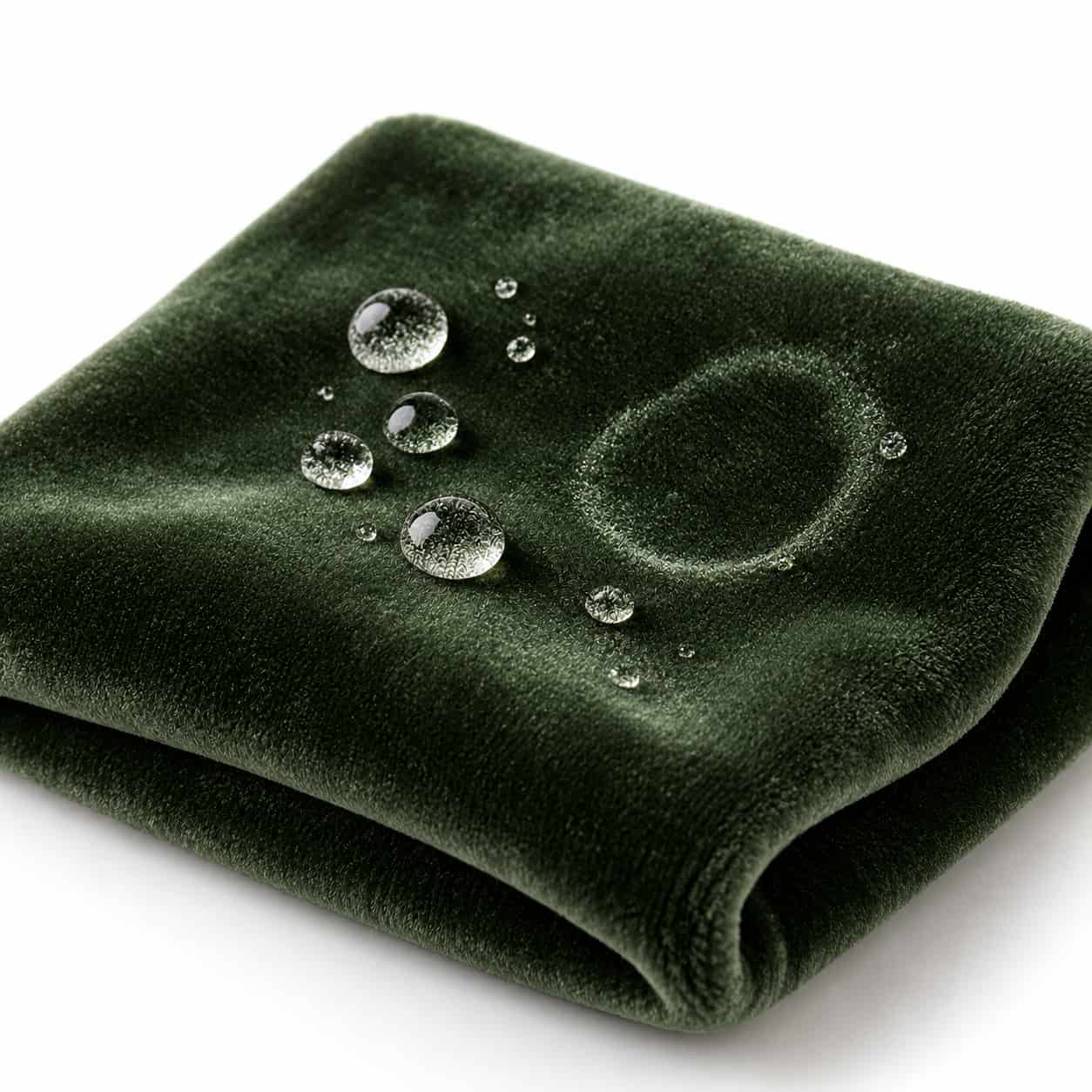 Nahaufnahme von dunkelgr&uuml;nem Samt mit Wassertropfen und einem getrockneten, hell schimmernden Wasserrand auf wei&szlig;em Hintergrund. Shikardos Reinigung entfernt Wasserr&auml;nder auf Samt in Frankfurt, indem die ganze Fl&auml;che gleichm&auml;&szlig;ig behandelt und der Flor danach ausgerichtet wird.