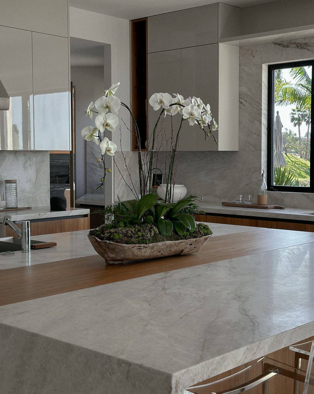 Orchid and moss centerpiece in a driftwood bowl on a marble kitchen island