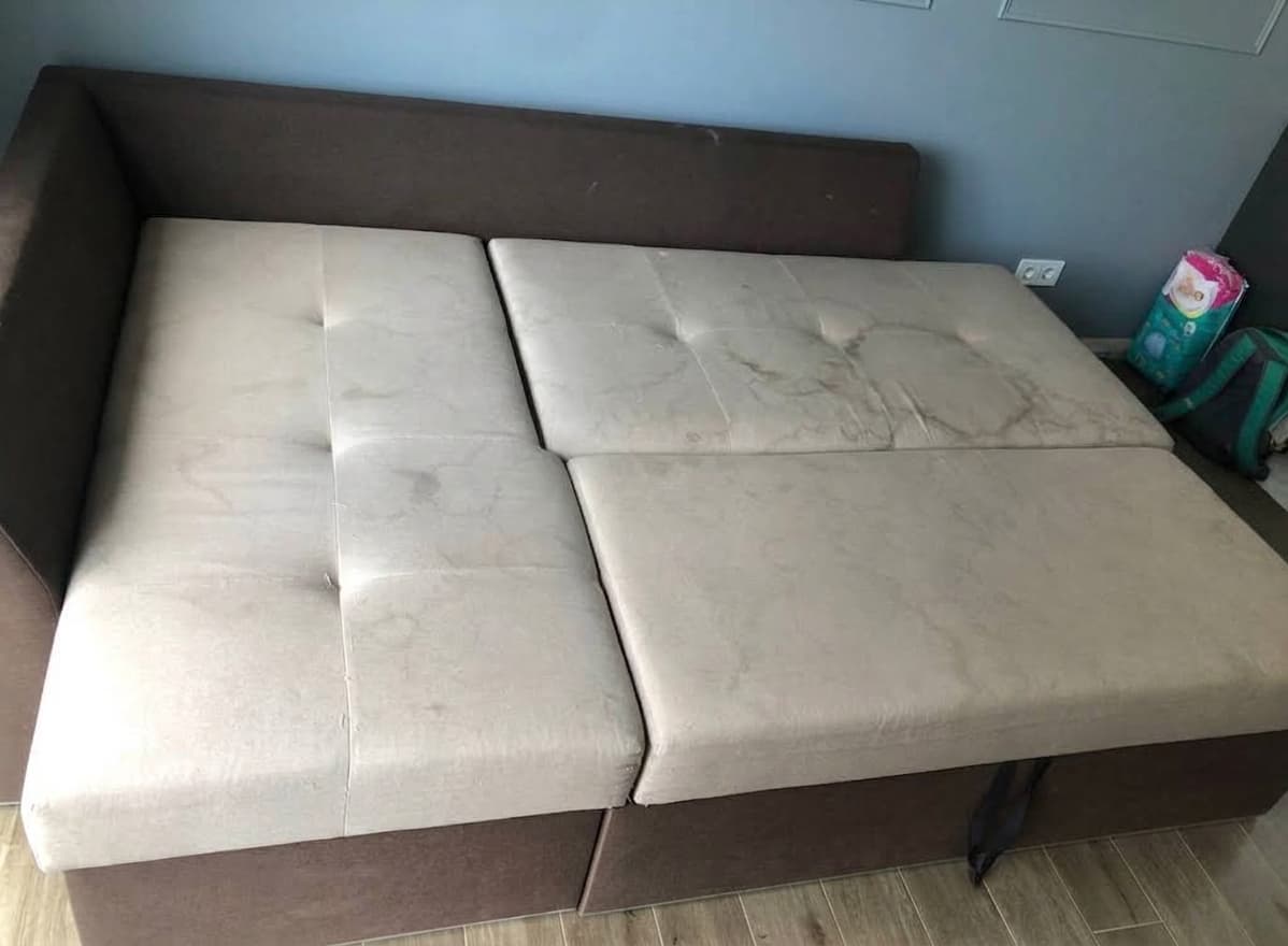 Helles Sofa eines Kunden aus Frankfurt vor der professionellen Reinigung, mit alten dunklen Flecken und sichtbaren Gebrauchsspuren auf Sitzfl&auml;che und Armlehne. Das Foto hat der Kunde selbst aufgenommen und seiner Google-Bewertung f&uuml;r Shikardos Reinigung beigef&uuml;gt.