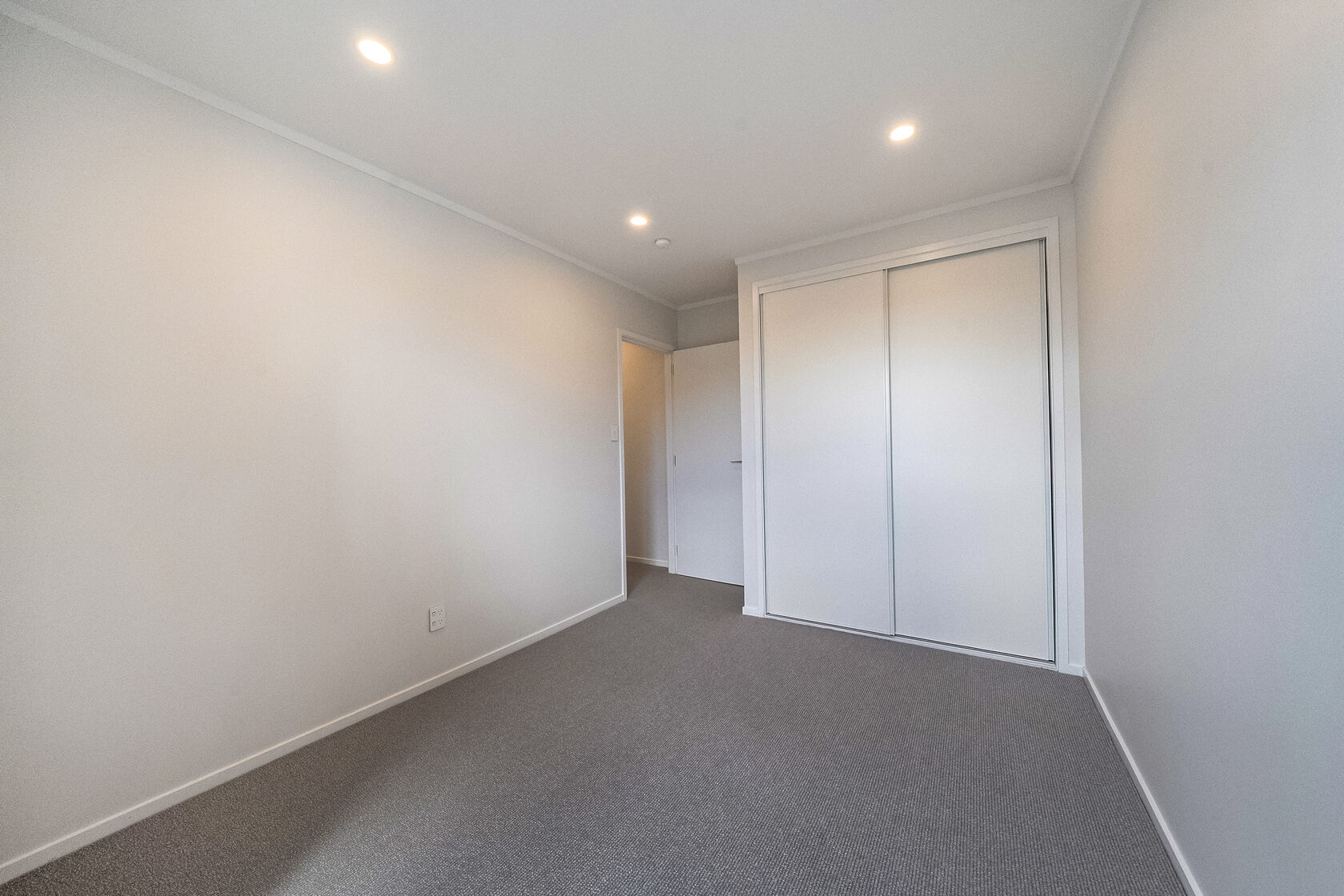 Empty bedroom with built-in sliding wardrobe, carpet flooring, and recessed ceiling lighting.