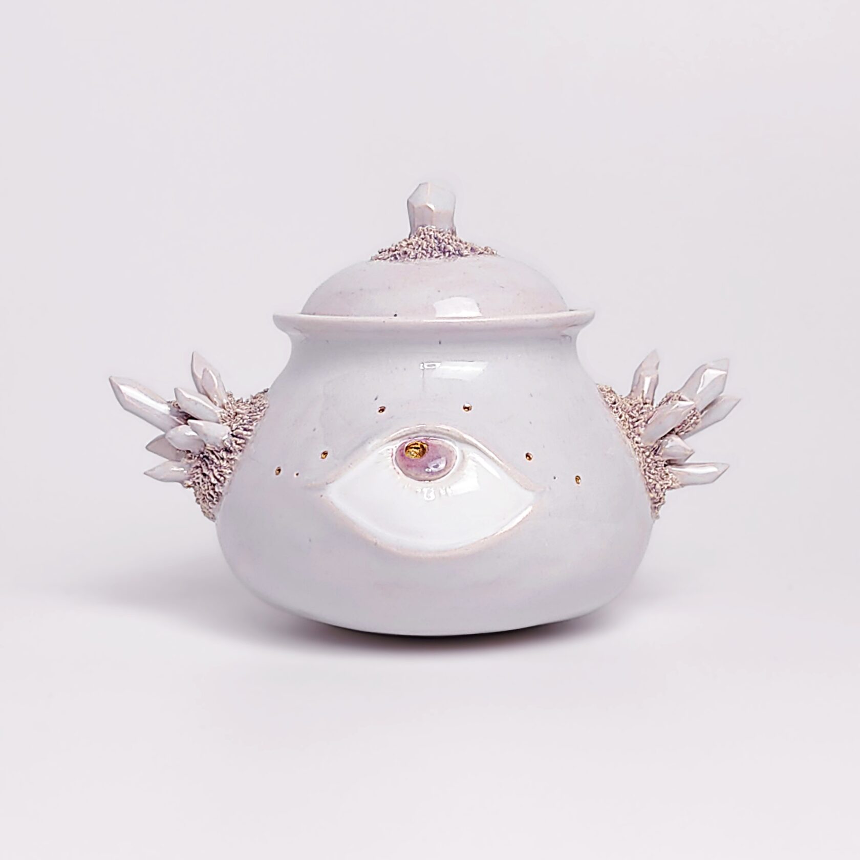 Unique handmade ceramic jar with a sculpted eye, textured crystal-like side elements, and soft pearlescent glaze