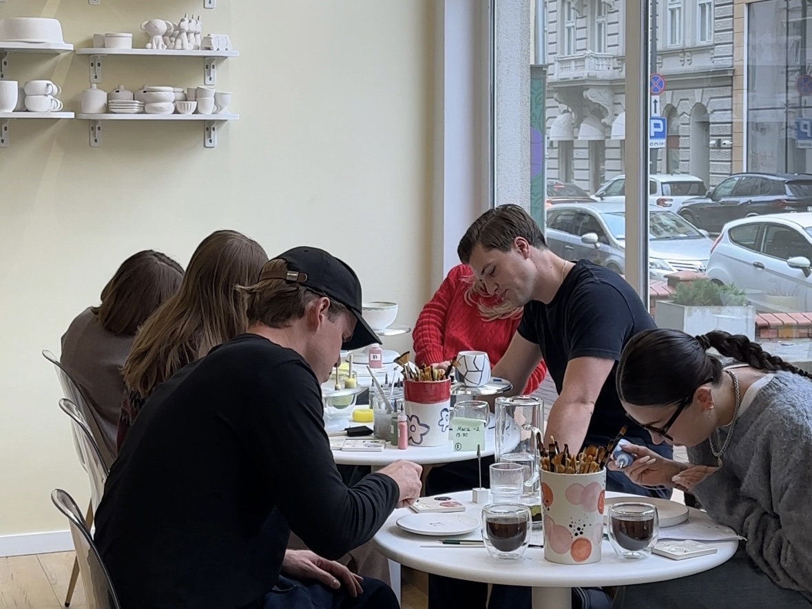 Zespół maluje ceramikę przy okrągłych stolikach w Create Cafe