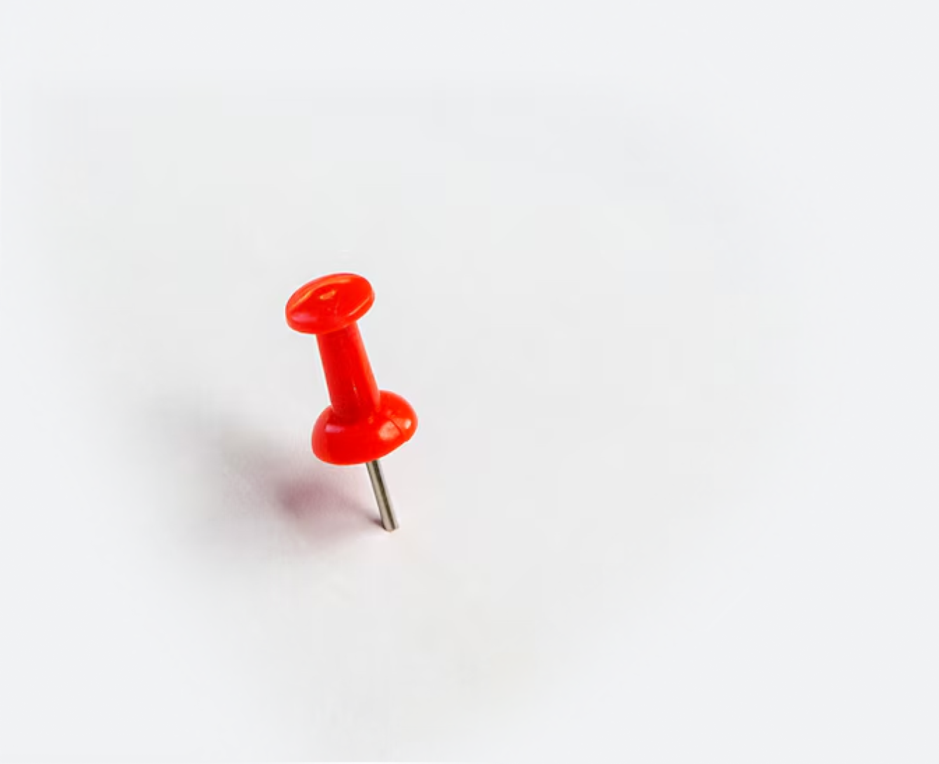 A solitary red pushpin, like a beacon to hire ruby developers, is placed on the lower-left corner of a plain white background. The sharp metal tip is visible amid ample empty white space, creating a minimalist composition.