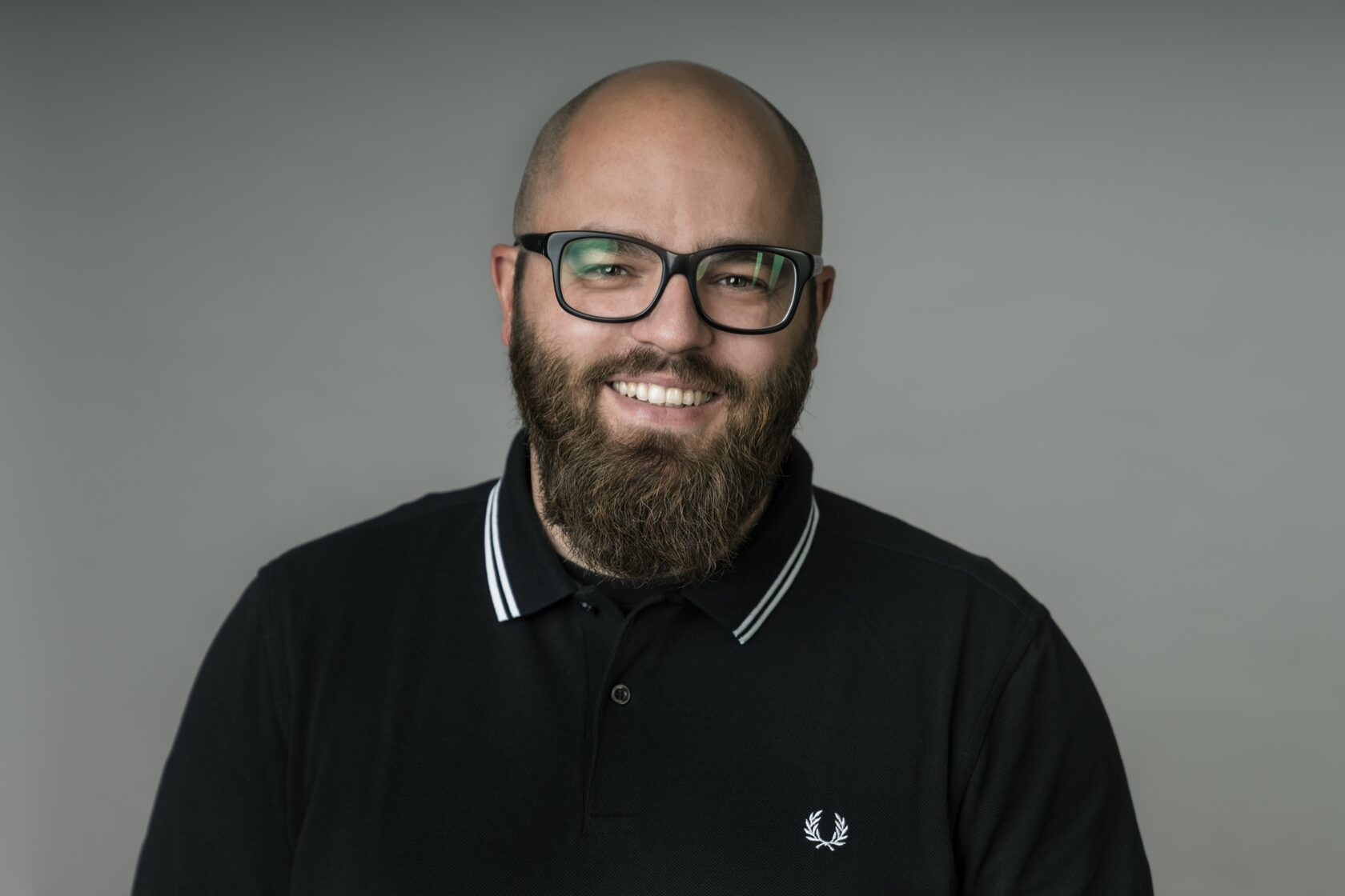 Businessportrait eines lächelnden Mannes mit Brille vor grauem Hintergrund – Evgenia Huber
