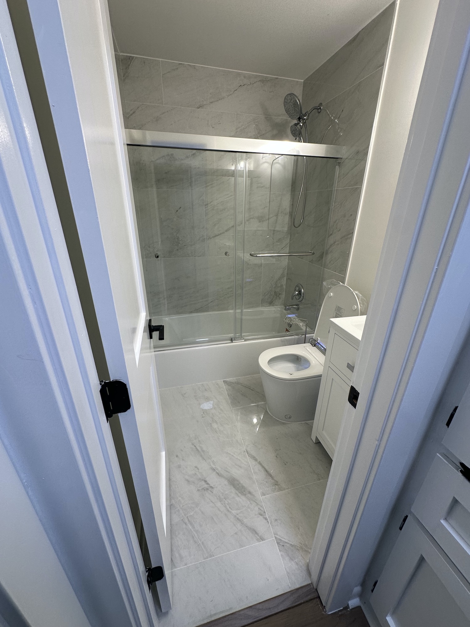 Bathroom entrance view showing large-format floor tile, tub, glass panel and smart toilet