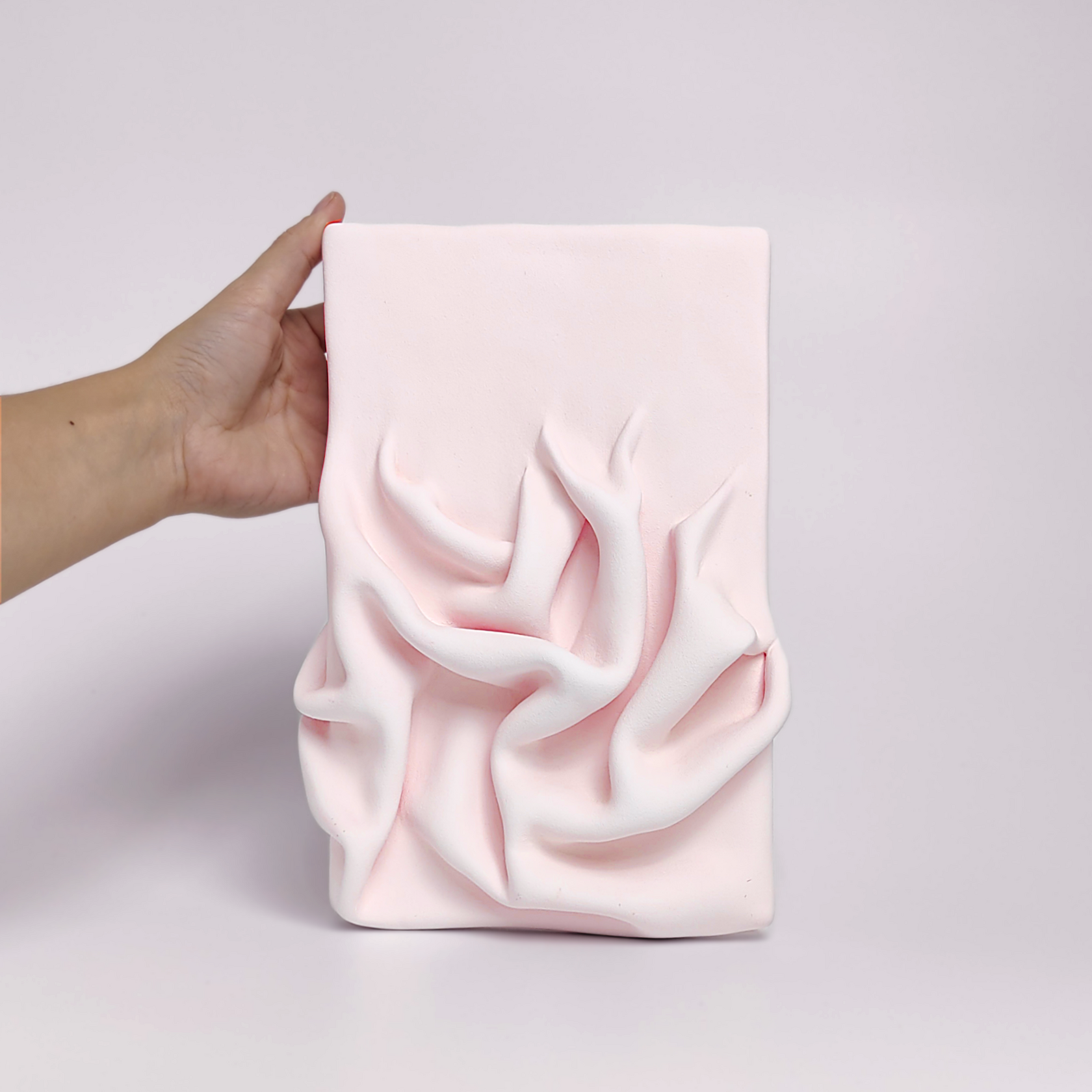 textured wall art made of air-dry clay in a soft pink shade with flowing sculpted drapery