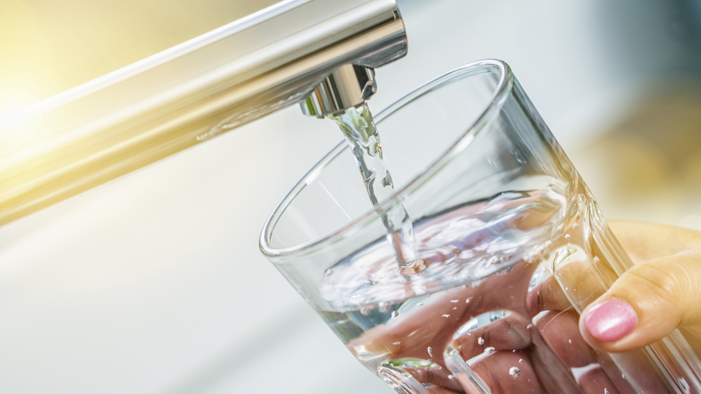 The image shows a glass being filled with purified water from a tap, illustrating the effectiveness of reverse osmosis in removing coliform bacteria and ensuring safe drinking water