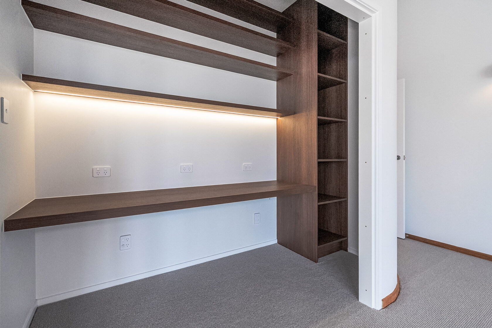Custom built-in study nook with floating timber desk, open shelving, and integrated LED strip lighting.