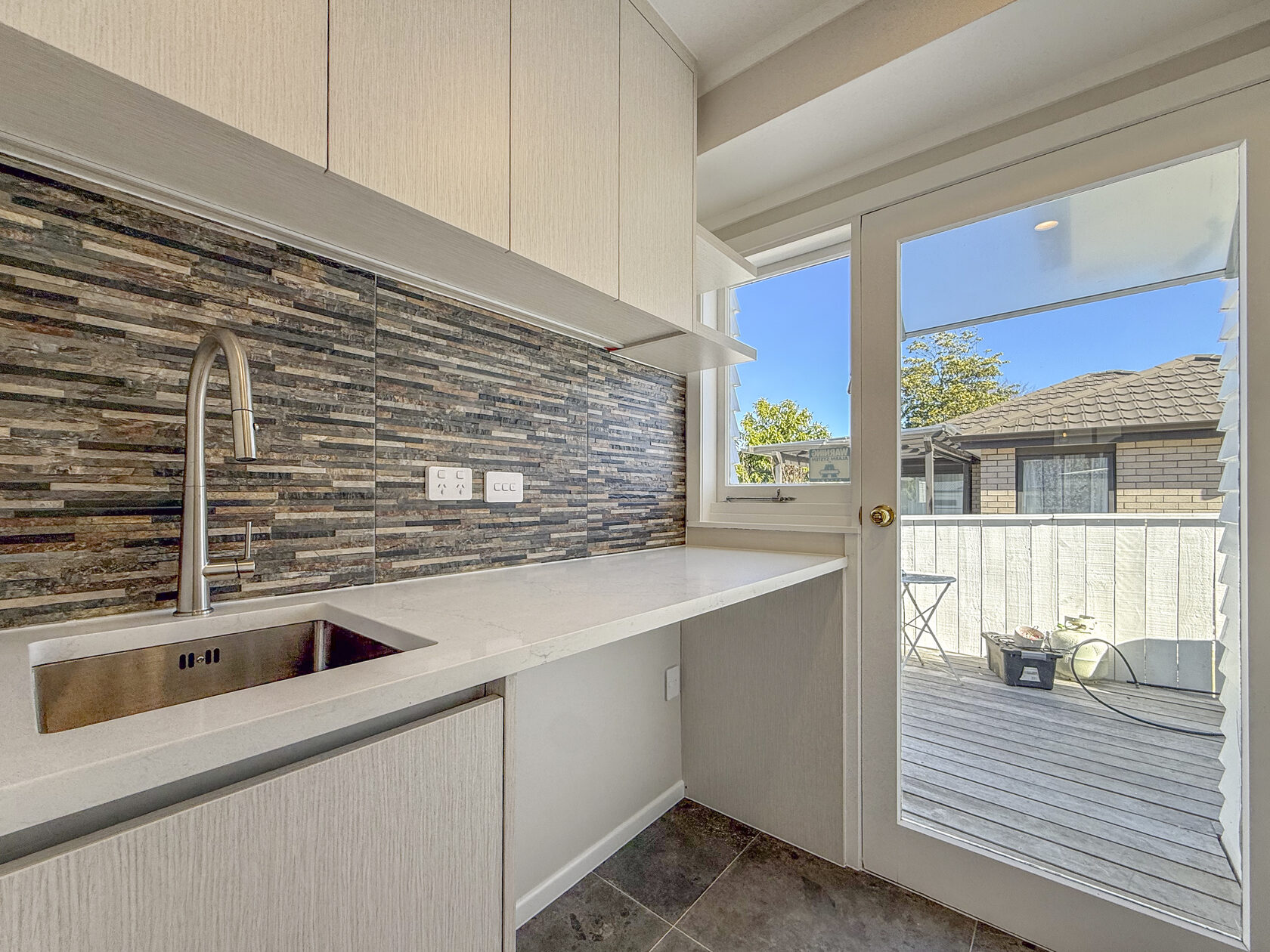 Laundry sink, white cabinets and patterned splashback beside a glazed exterior door