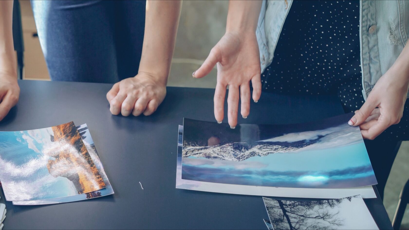 Zwei Personen vergleichen an einem Tisch ausgedruckte Fotos und prüfen, welches Bild sie nehmen.